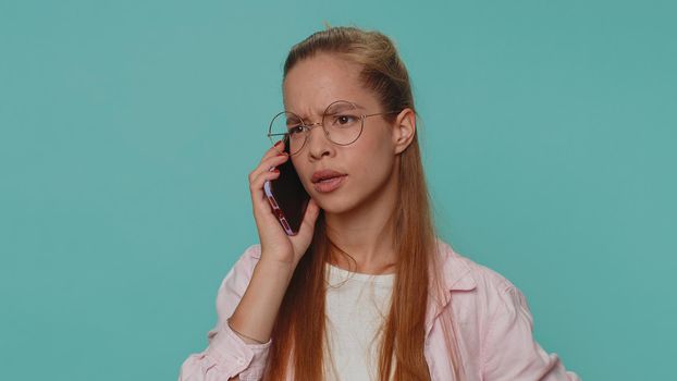 Tired teenager student girl making online conversation speaks on smartphone. Boring call. Blah expression. Nonsense talk. Young stylish teen female child kid isolated alone on blue studio background