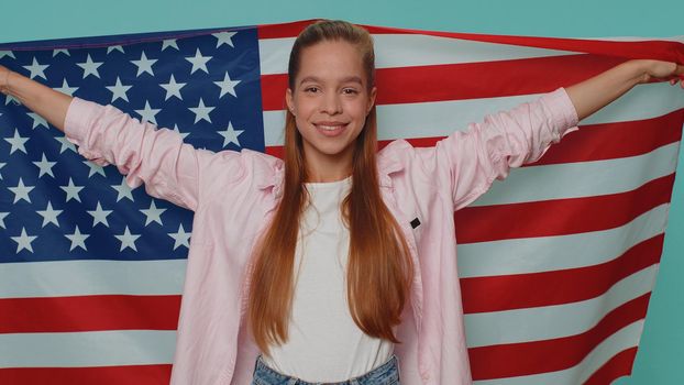 Lovely teenager girl waving and wrapping in American USA flag, celebrating, human rights and freedoms. Independence day. Young stylish child kid isolated alone on blue studio background indoors