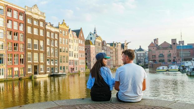 Amsterdam Damrak during sunset, happy couple man and woman on a summer evening at the canals, a dutch couple at Waterfront by Dancing house of Amsterdam during a summer evening in Amsterdam