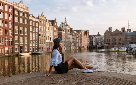 Amsterdam Damrak during sunset, happy woman on a summer evening at the canals, a Asianwomen at Waterfront by Dancing house of Amsterdam during a summer evening in Amsterdam