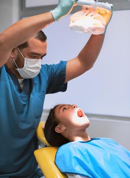 Shining brightly. a young little girl lying down on a dentist chair with her mouth wide open while the dentist shines a light on her