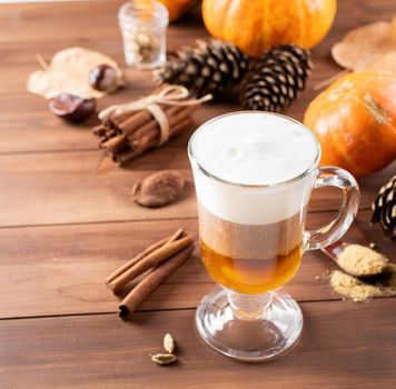 Autumn hot drinks. Pumpkin spice latte in a glass mug with cinnamon and ginger on wooden background with copy space