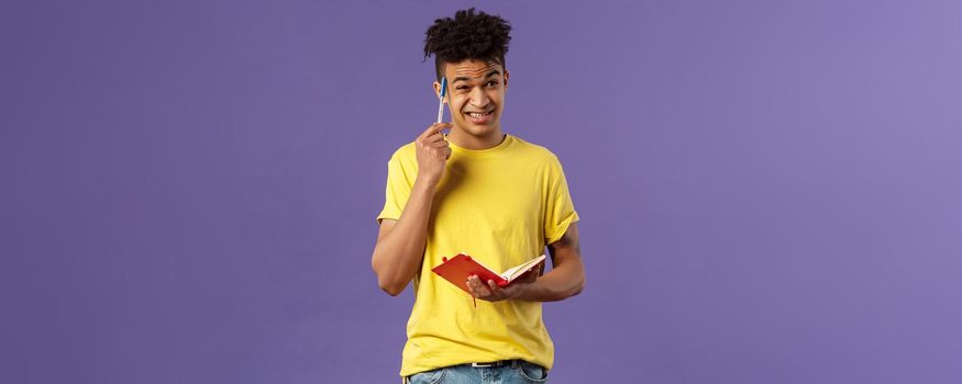 Young troubled male student studying, doing homework, scratch head indecisive and unsure, facing complicated task, dont know how solve equation, grimacing, holding notebook, thinking.