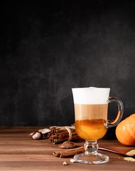 Autumn hot drinks. Pumpkin spice latte in a glass mug with cinnamon and ginger on dark background with copy space