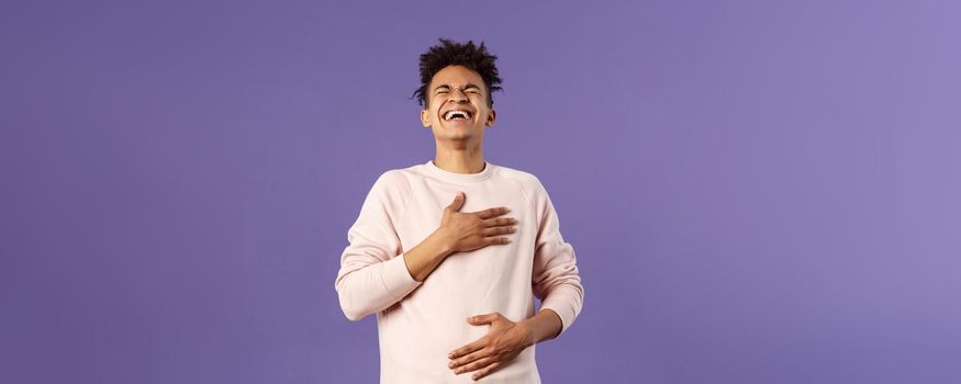 Portrait of cheerful, happy young hipster guy laughing out loud from hilarious joke, watching awesome stand-up performer, chuckle and touchign chest, bending backwards from laugh.