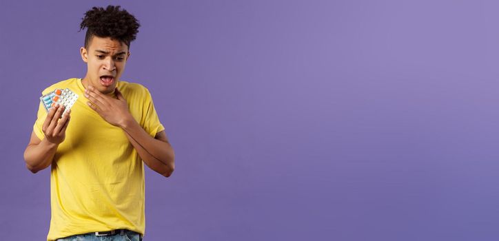 Health, influenza, covid-19 concept. Portrait of young man coughing, choking with tablet, drank pill without water, holding drugs and touch neck as suffer sore throat, purple background.