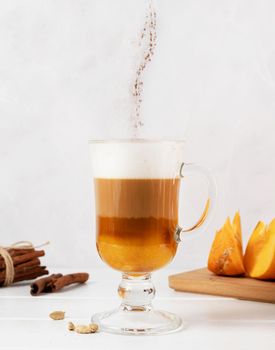 Autumn hot drinks. Pumpkin spice latte in a glass mug with cinnamon on light background with copy space. cinnamon powder falling