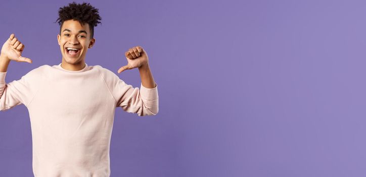 Portrait of confident young upbeat man, smiling bragging, being boastful about own accomplishments, indicate himself with proud rejoicing face, standing purple background.