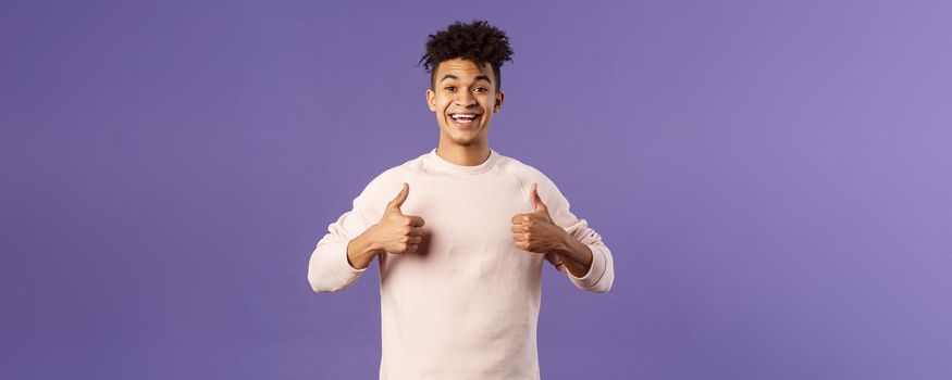 Portrait of upbeat, happy smiling man left pleased after using company service, studying at online language school, show thumbs-up and look camera, recommending, stand purple background.