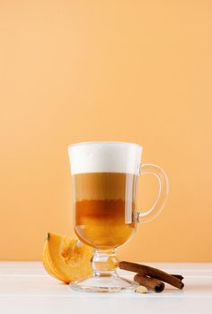 Autumn hot drinks. Pumpkin spice latte in a glass mug with cinnamon on orange background with copy space