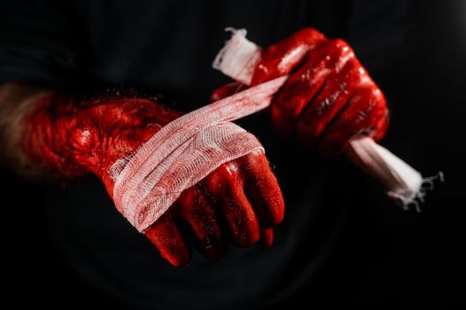 A man covered in blood bandages his hands