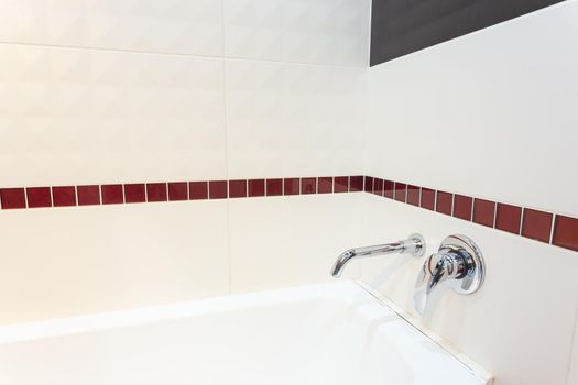 White acrylic bathtub with built-in wall mixer. The wall is lined with ceramic tiles.