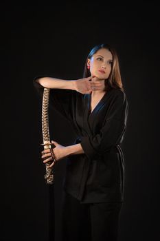 Vertical portrait of a pensive young brunette woman with a katana on a black background.
