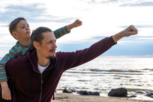 father and son superheroes. a happy father holds his son on his back. they raised their fist up and forward. movement to victory.