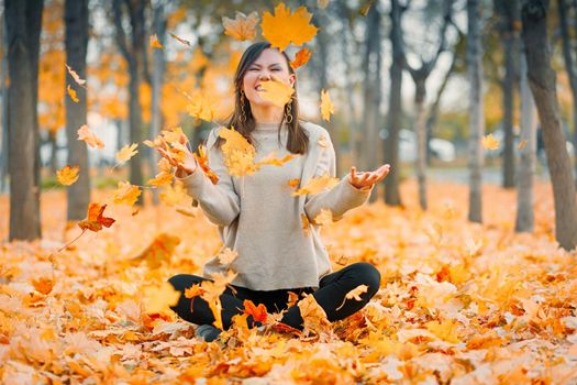 Happy fall young woman smiling joyful throws up autumn leaves outside in yellow fall forest. Beautiful mixed race Caucasian, Central Asian woman.