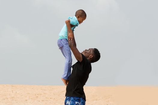 young man lifting his little brother to the beach.