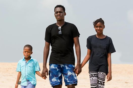 a young man with his children at the beach walking back to the sea hands in hands.