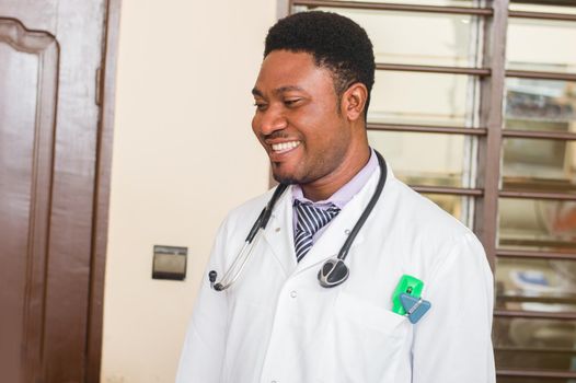 Smiling medical doctor in white coat with a stethoscope standing in his office.