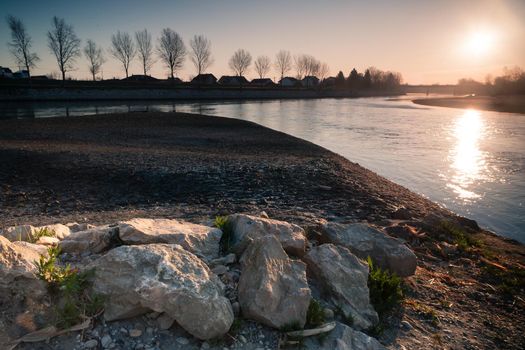 Sunrise by the river Drava. Closeup white stones. An idyllic sunrise in nature. Landscape photo of sunrise with sun the right upper corner, white stones in a front and a river in a middle. Croatia.