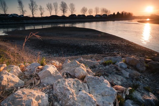 Sunrise by the river Drava. Closeup white stones. An idyllic sunrise in nature. Landscape photo of sunrise with sun the right upper corner, white stones in a front and a river in a middle. Croatia.