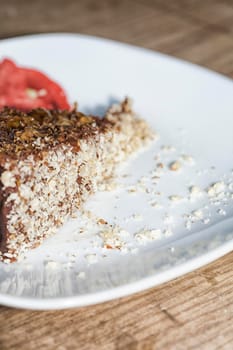 Close up view of a skice of brown, chocolate cake on a white plate. Chocolate crumbs can be seen on the plate.