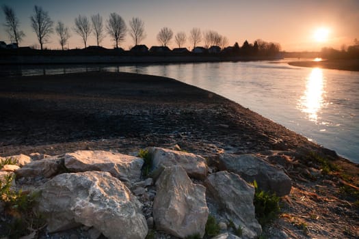 Sunrise by the river Drava. Closeup white stones. An idyllic sunrise in nature. Landscape photo of sunrise with sun the right upper corner, white stones in a front and a river in a middle. Croatia.