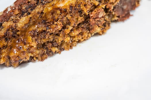 Close up view of a skice of brown, chocolate cake on a white plate. Chocolate crumbs can be seen on the plate.