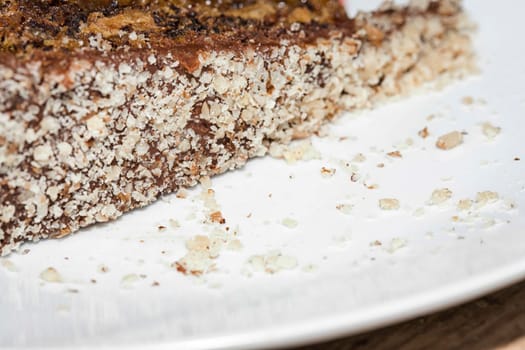 Close up view of a skice of brown, chocolate cake on a white plate. Chocolate crumbs can be seen on the plate.