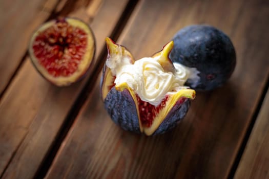 Fresh sliced purple figs with whipped cream on a wooden background from old boards. Raw exotic figs. Low key