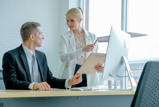 Young beautiful secretary discuss with her boss about their work in front of glass window and computer.