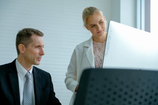 The manager look to computer screen and young secretary stand near him.