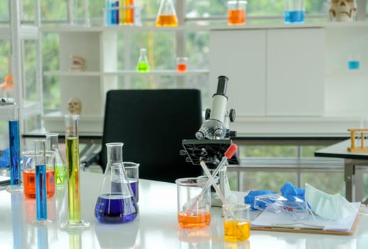 The microscope is put on desk with various glassware of science working.