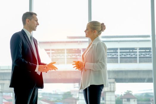 Business man stands and discuss with young beautiful woman in the room with glass windows.