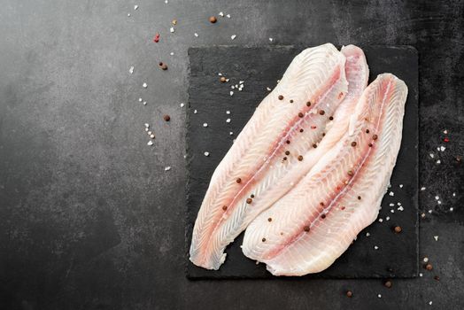 Fresh raw white fish fillet Pangasius with spices and lemon on state plate on a stone background with copy space for your text