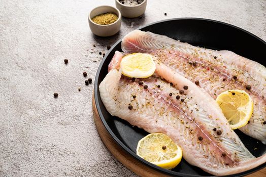Fresh raw white fish fillet Pangasius with spices and lemon in frying pan on a stone background with copy space for your text