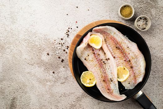 Fresh raw white fish fillet Pangasius with spices and lemon in frying pan on a stone background with copy space for your text