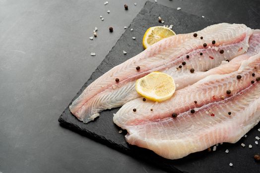 Fresh raw white fish fillet Pangasius with spices and lemon on state plate on a stone background with copy space for your text