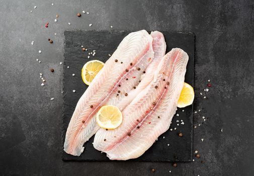 Fresh raw white fish fillet Pangasius with spices and lemon on state plate on a stone background with copy space for your text