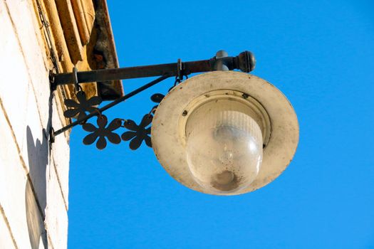An old lamp hangs on the building against a blue sky