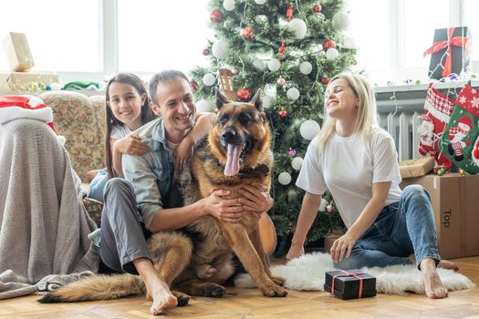 smiling family and daughter with dog sitting near christmas tree with gifts.