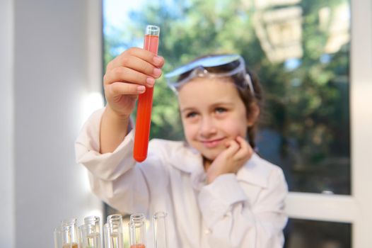 Details: hands of a little girl wearing protective workwear and safety lab goggles, future chemist scientist observing the test tube with going chemical reaction with fascination and excitement