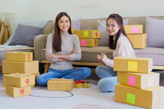 Portrait of Starting small businesses, two Asian woman check online orders Selling products working with boxs freelance work at home office, sme business concepts