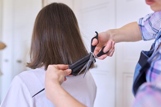 Mother cutting hair to teen daughter, beauty and care at home.