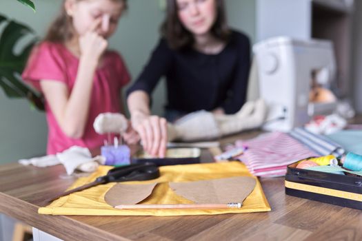 Family creative handmade hobby and leisure, children sitting at home, sewing doll, in defocus, background. Close-up of fabric, templates, patterns, scissors, threads, needles