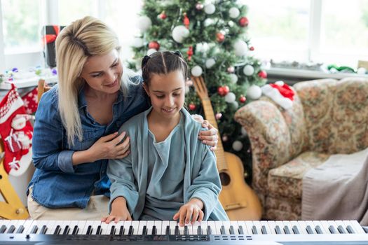 Mom teaching her daughter to play a new year song on the piano on christmas eve in a decorated room, new year mood.