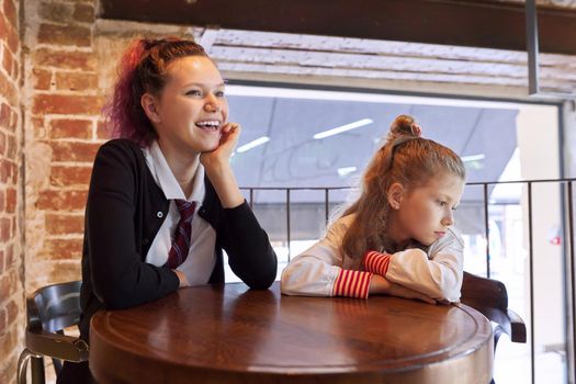 Children, two sisters, teenager and younger sister, sitting together in cafe at table. Girls resting after school