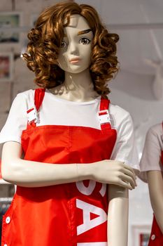 beautiful mannequin girl in a seller's apron with red hair in a clothing store. shopping, fashion, style. Standing woman dummies show collection of clothes