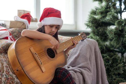 Child playing the guitar and singing near a christmas tree.
