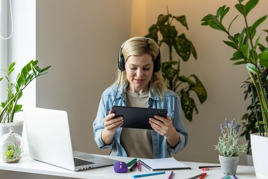 Image of young pleased happy cheerful cute beautiful business woman sit indoors in office using laptop computer listening music with earphones.