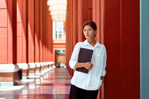 Businesswoman portrait. Caucasian female business person standing outdoor with business paper document holder. Young beautiful modern business woman 30s years. Confidence employer. Looking at camera